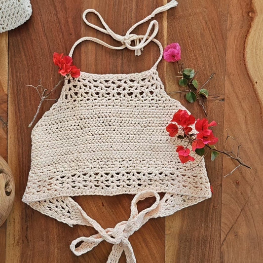 Light pink crocheted top on wooded table with red flowers as decoration