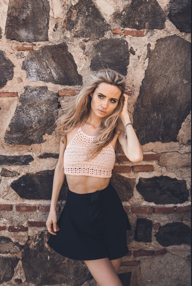 Girl wearing crocheted Anna Algarve top in light pink with stone wall in background. Castle Solhail