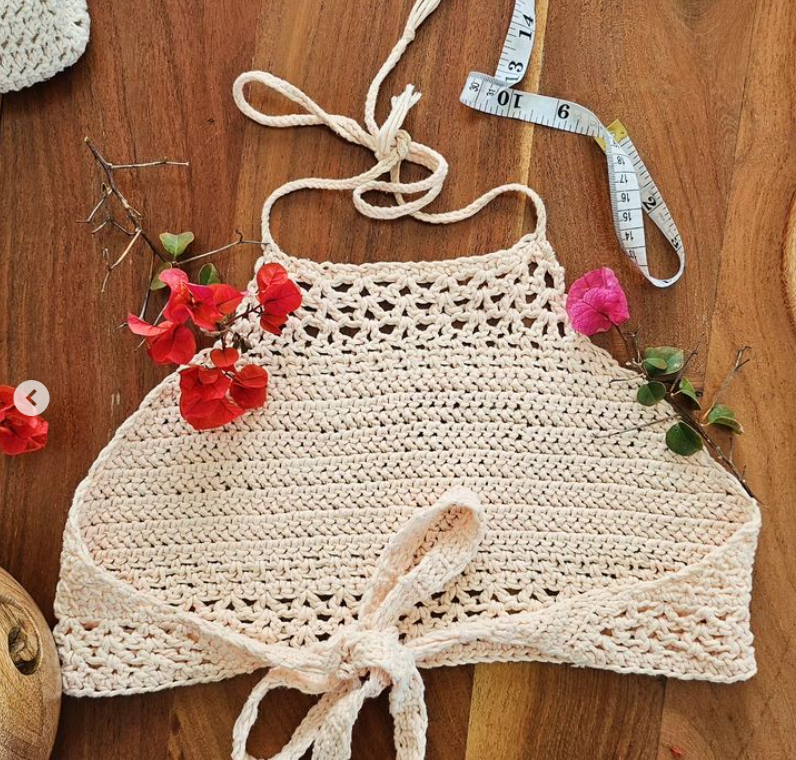 Light pink crocheted top on wooded table with red flowers as decoration